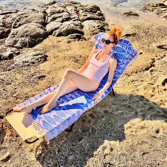 A person relaxing on a beach chair covered with a blue and white geometric patterned Beachable towel.