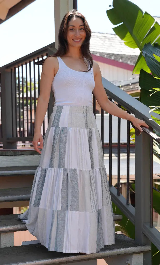 Woman wearing a maxi length tiered skirt with charcoal, grey and white stripes with a white tank top outside