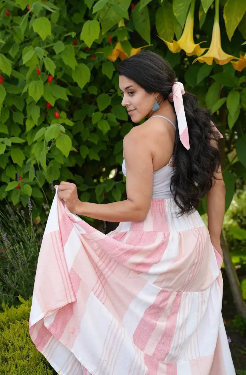Back View of a Woman wearing a maxi length tiered skirt with peach, salmon and white stripes with a white tank top outside
