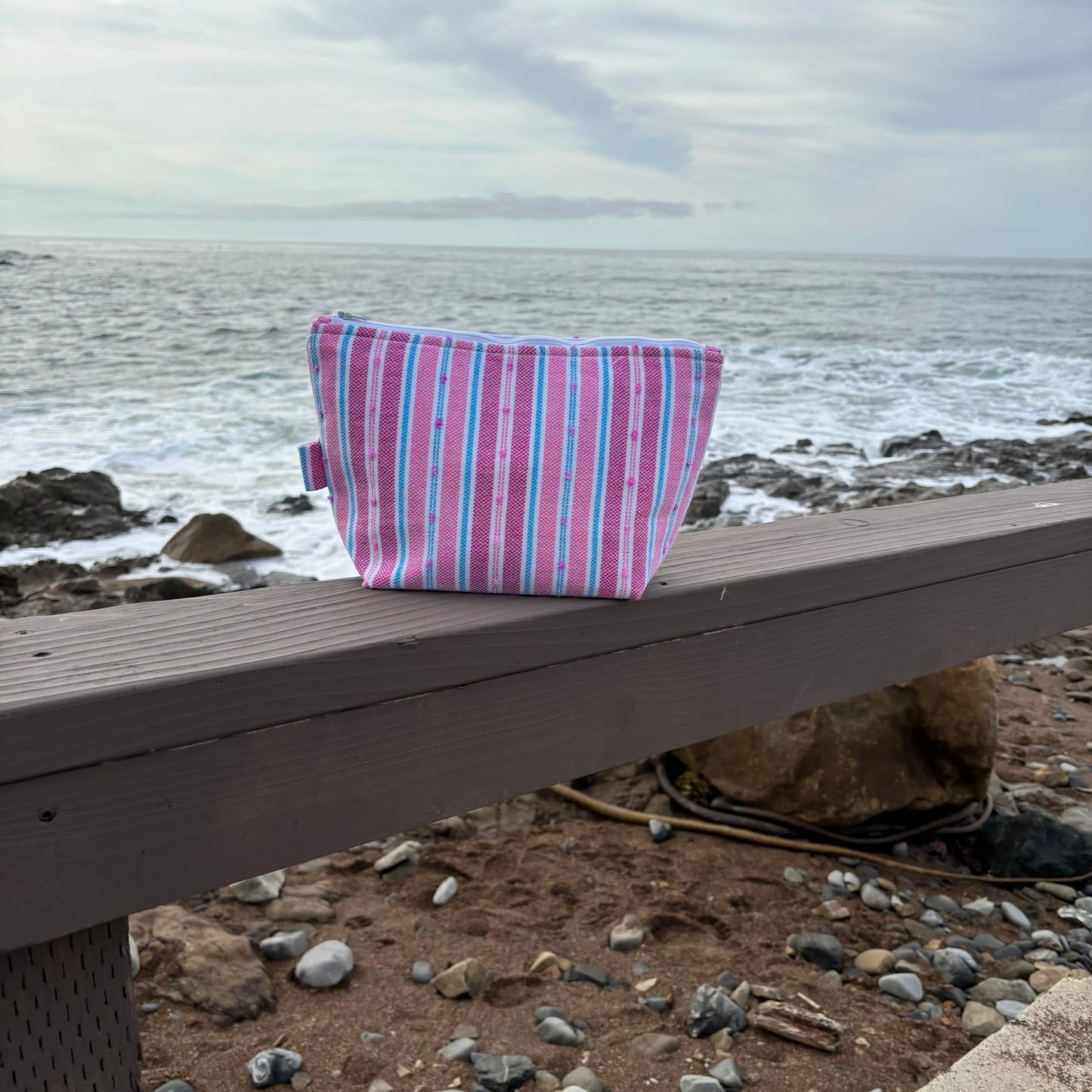 Pink and blue striped bag on a wooden bench by the ocean