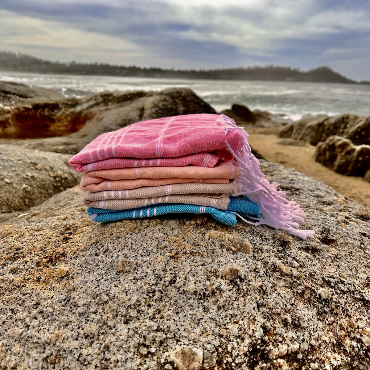 stack of folded towels on sandy beach with ocean background