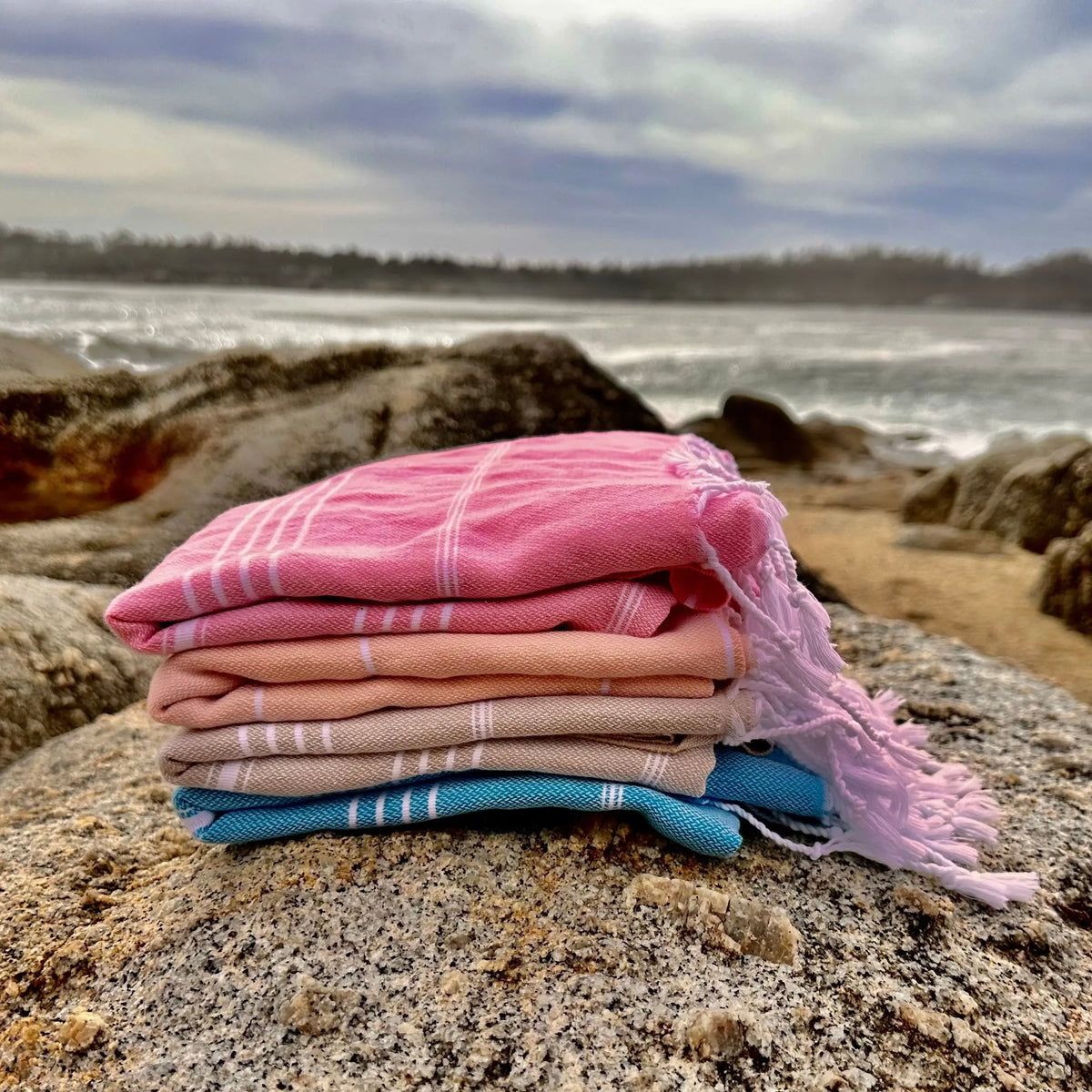 Stack of colorful towels on a rock with ocean and sky in the background