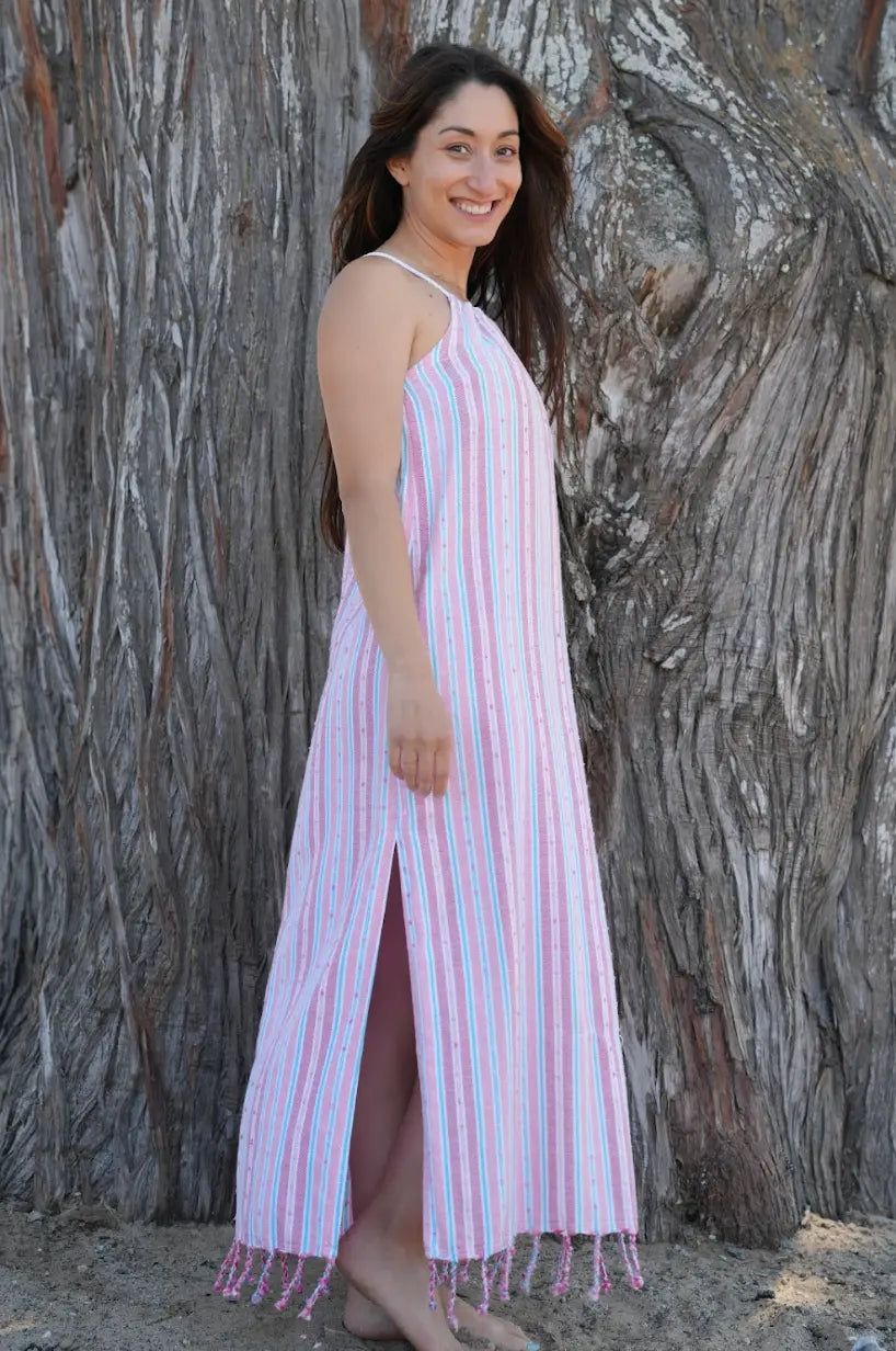 Woman in a pink striped dress standing against a tree trunk