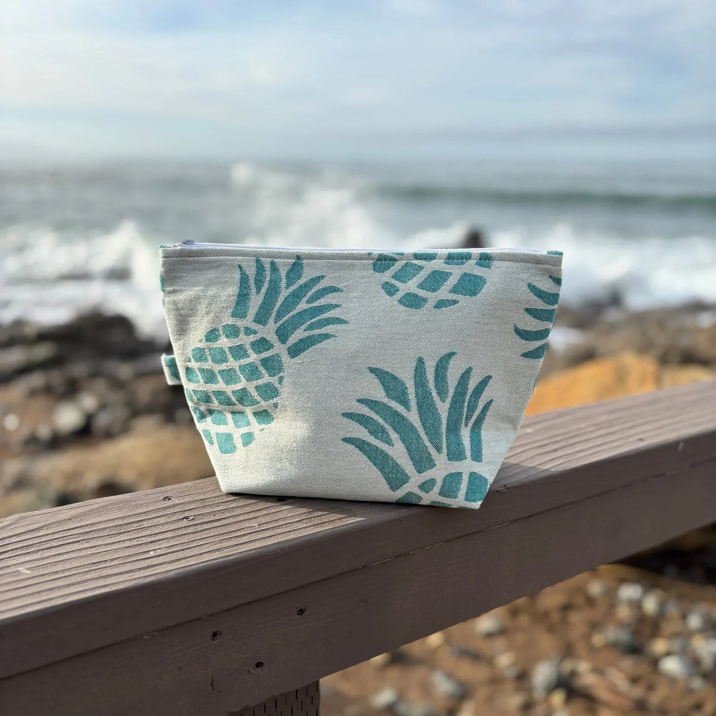 Fabric pouch with pineapple pattern on a wooden bench by the sea