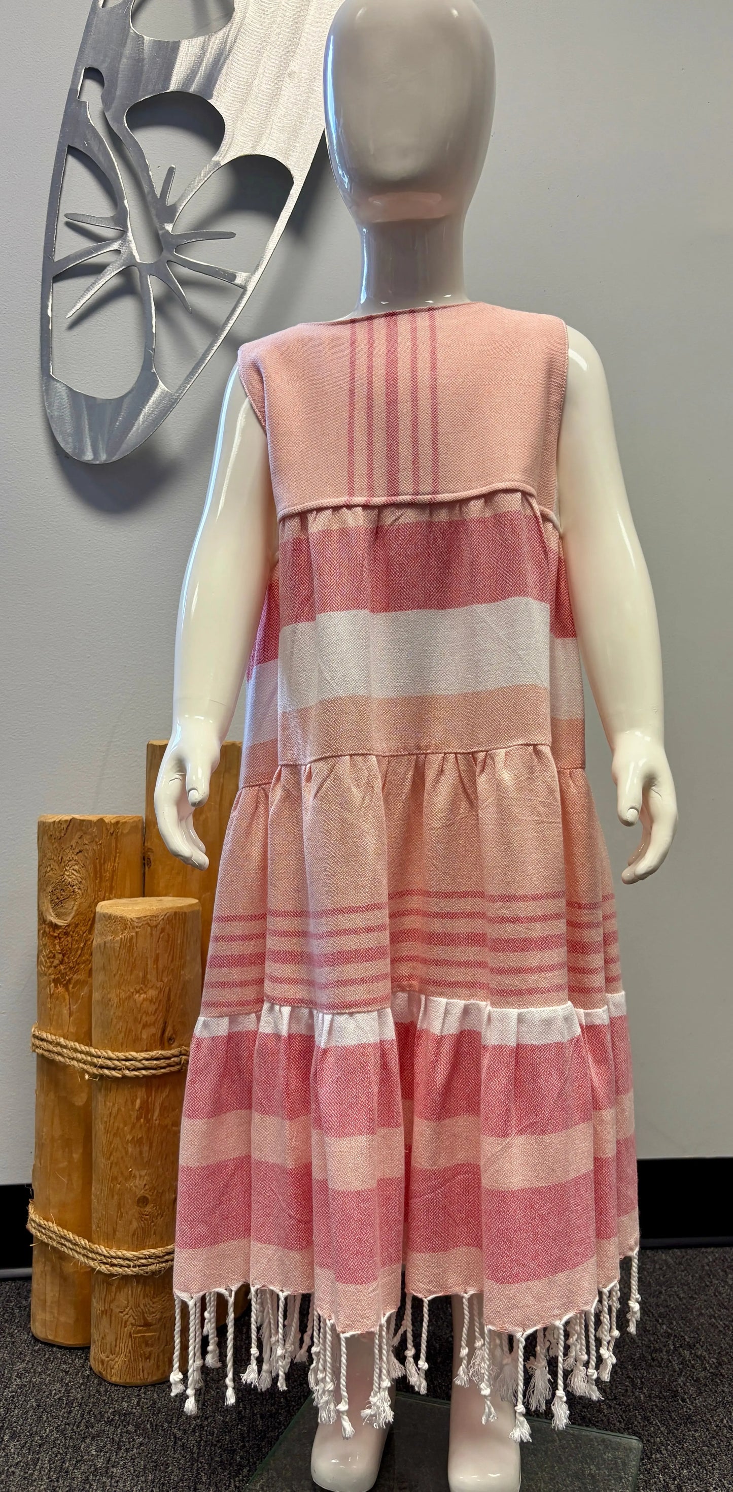 Mannequin wearing a peach, white and white striped dress with fringe details against a gray wall.