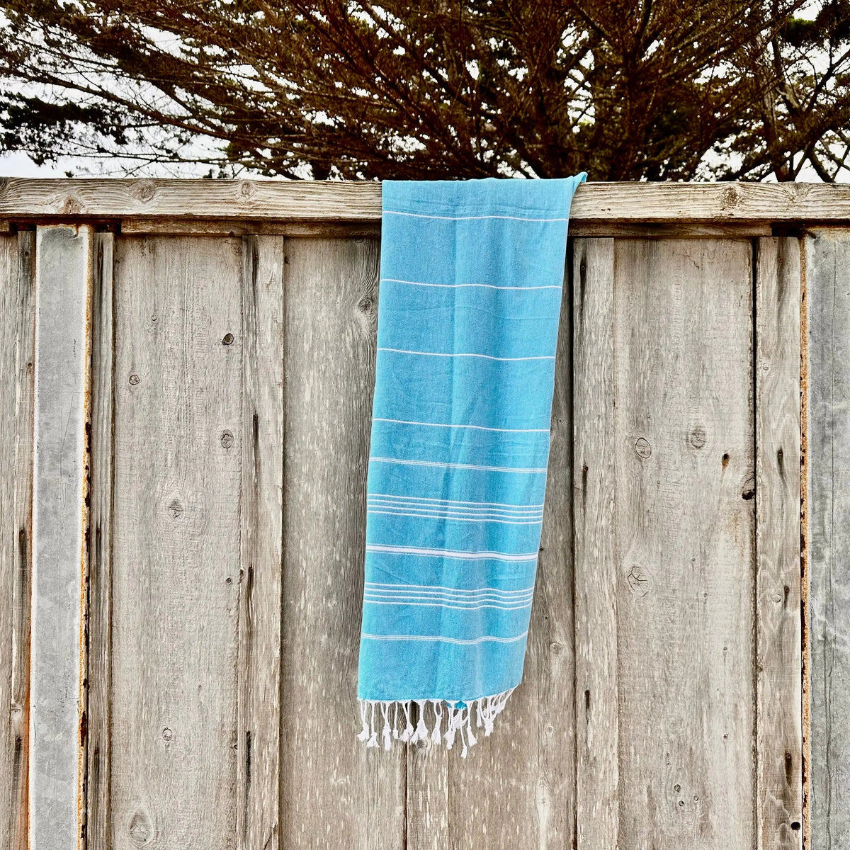 a blue Turkish cotton towel hanging over a wooden fench