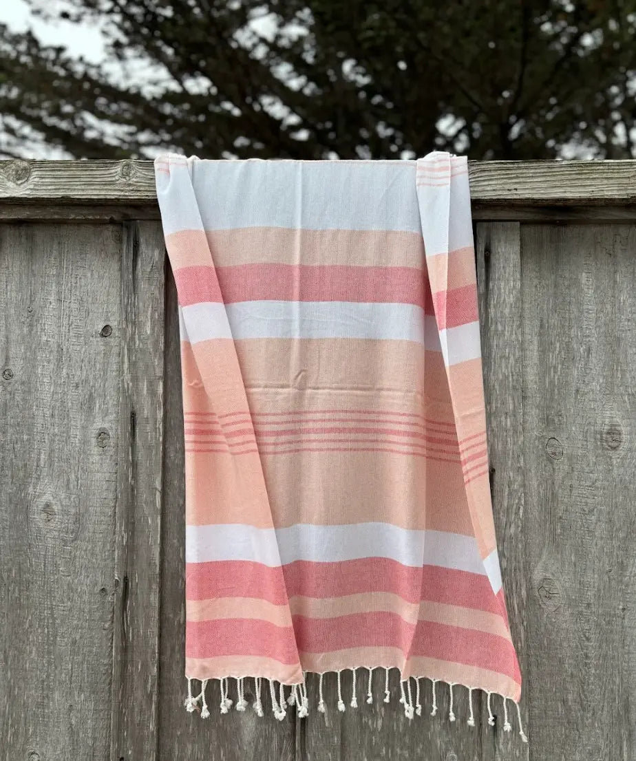 Peach, Salmon and White striped towel with tassels hanging on wooden fence