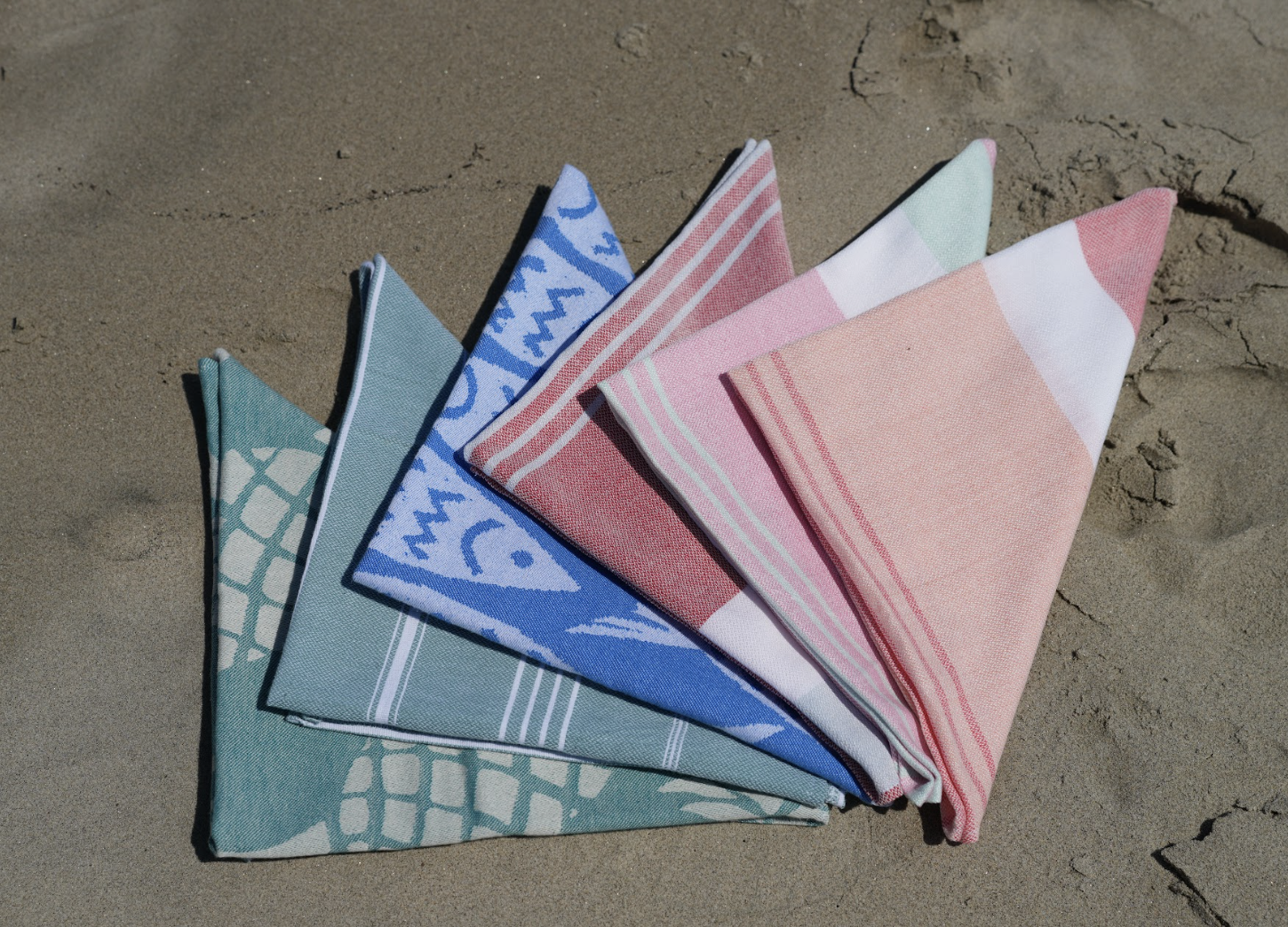 Several assorted colored folded bandanas arranged in a fan on the sand