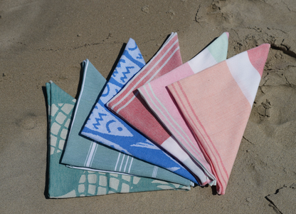 Several assorted colored folded bandanas arranged in a fan on the sand