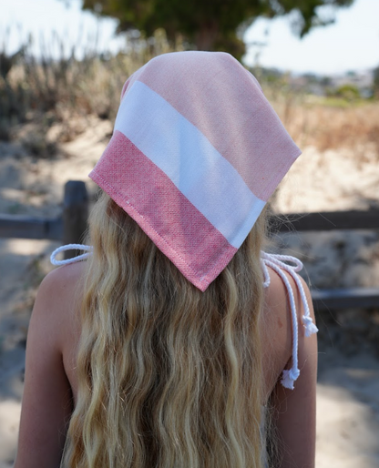 Back view of a red, peach and white striped  bandana being worn as a headband on a young girl