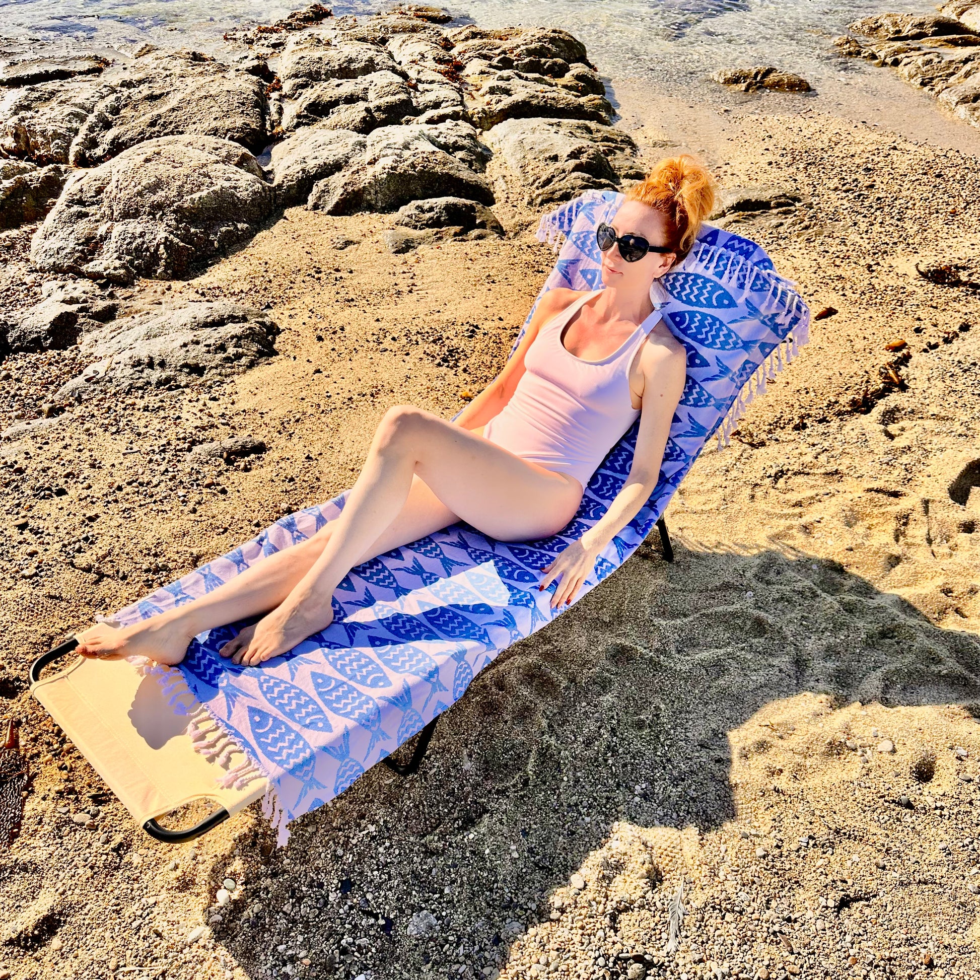 A person relaxing on a beach chair covered with a blue and white geometric patterned Beachable towel.