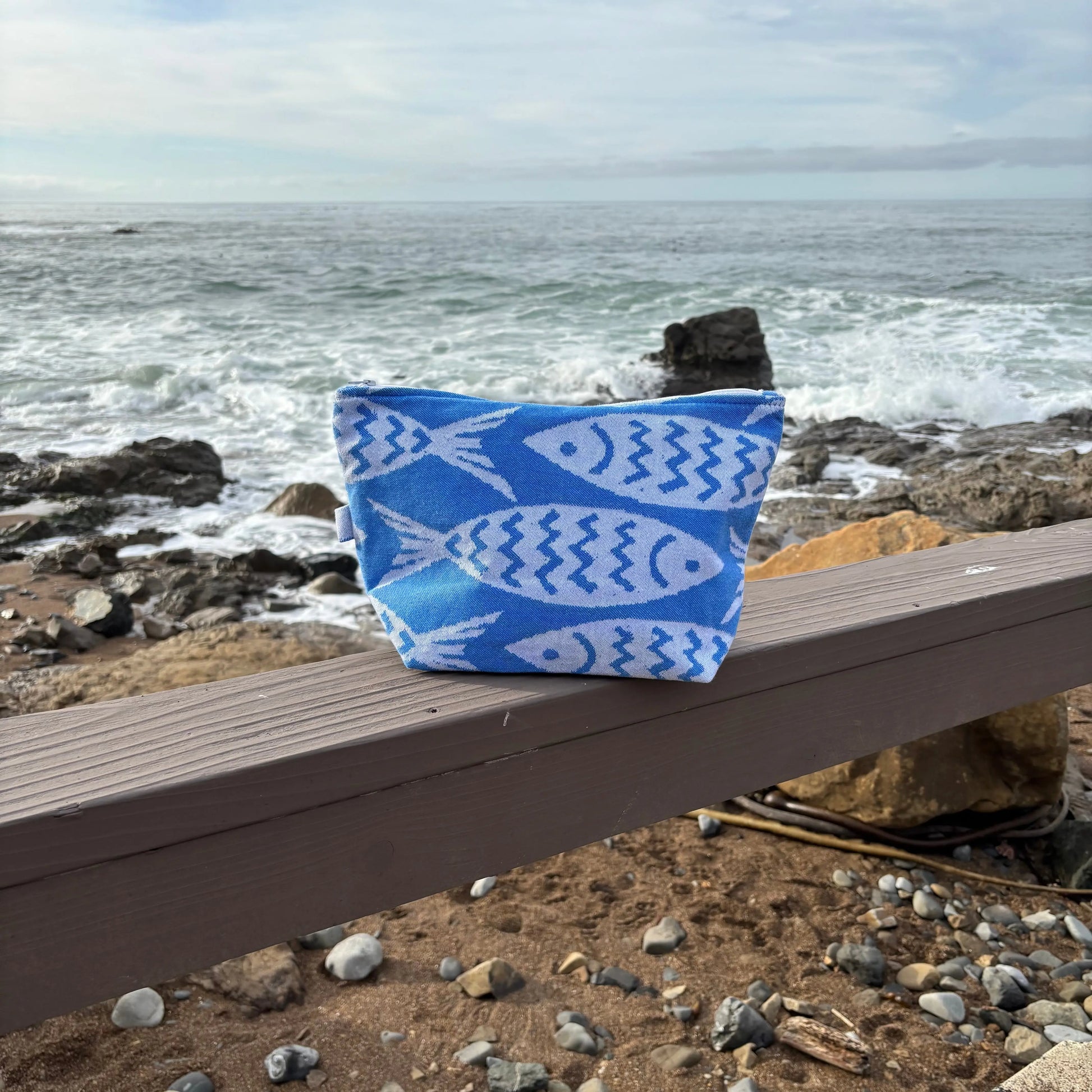 Blue and white fish patterned bag on a wooden bench by the ocean