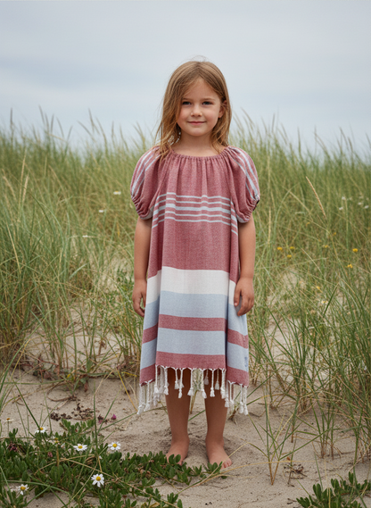Young girl in a red white and blue striped dress with tassels standing  near sand dunes
