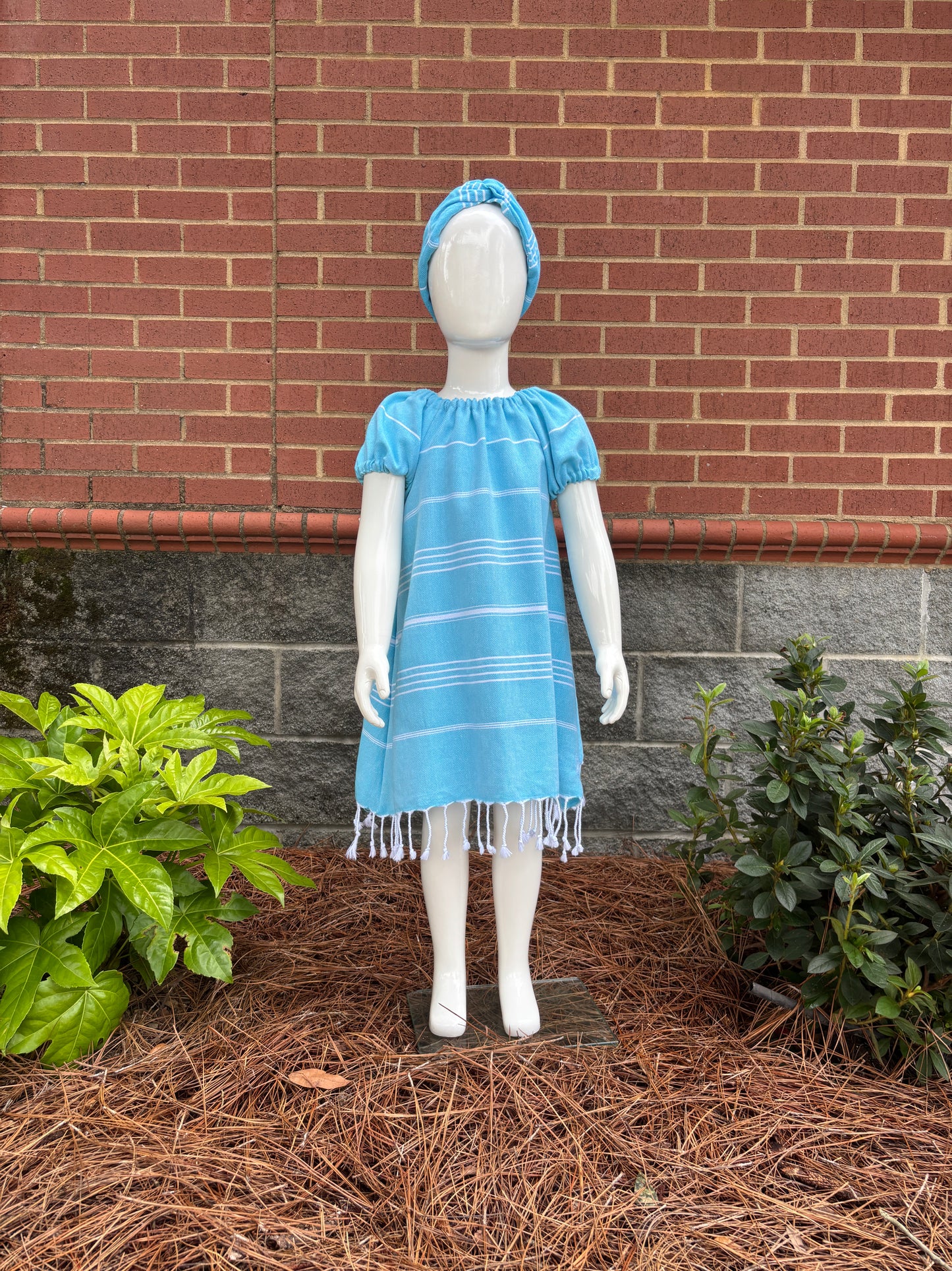 Mannequin wearing  blue striped dress with puff sleeves and tassels at hem in front of red brick wall