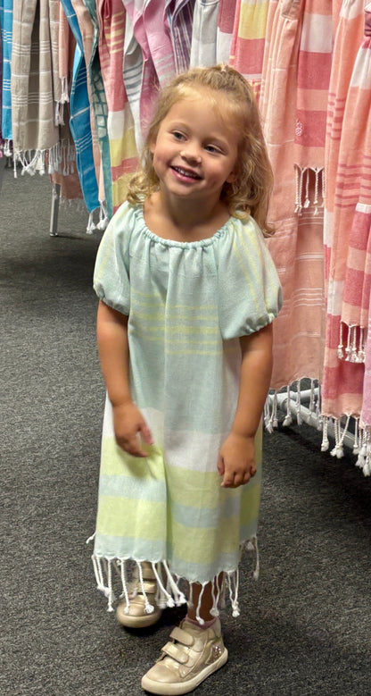 Young girl in green striped dress with puff sleeves and tassels at hem in store setting