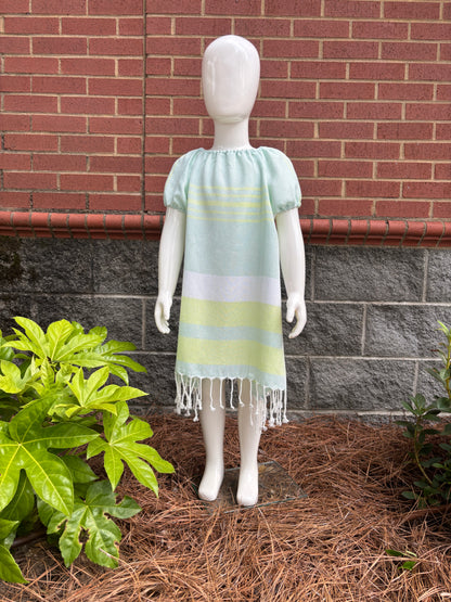 Mannequin wearing  green and white striped dress with puff sleeves and tassels at hem in front of red brick wall