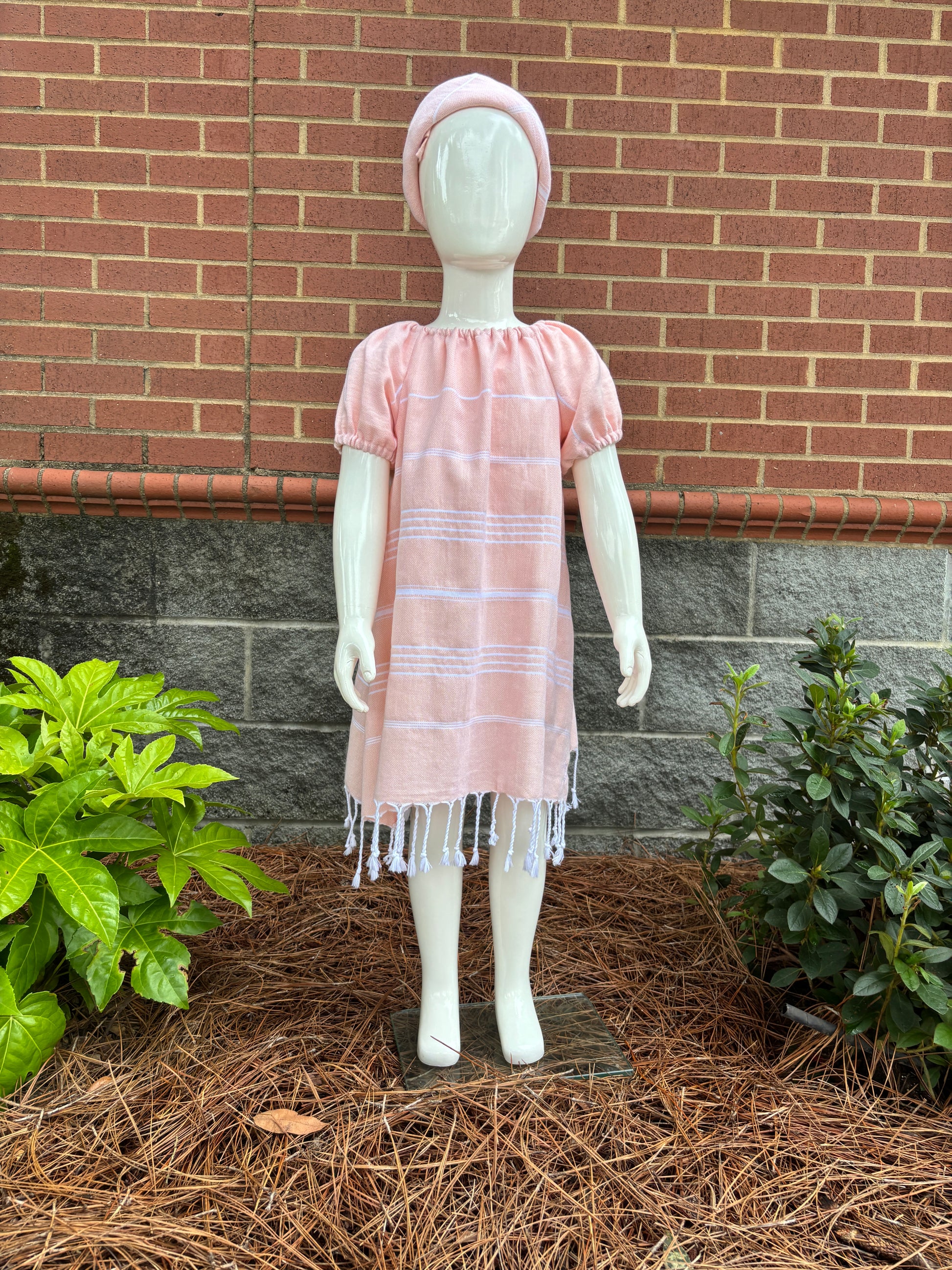 Mannequin wearing  peach striped dress with puff sleeves and tassels at hem in front of red brick wall