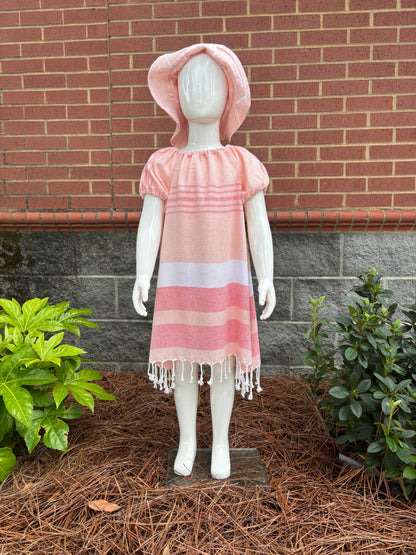Mannequin wearing  peach, red and white striped dress with puff sleeves and tassels at hem in front of red brick wall