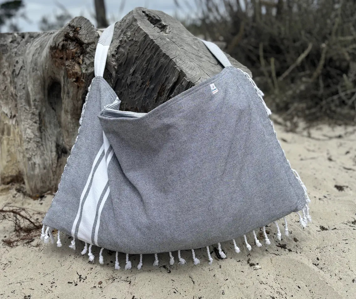 Gray bag with white stripes and fringes on a sandy surface