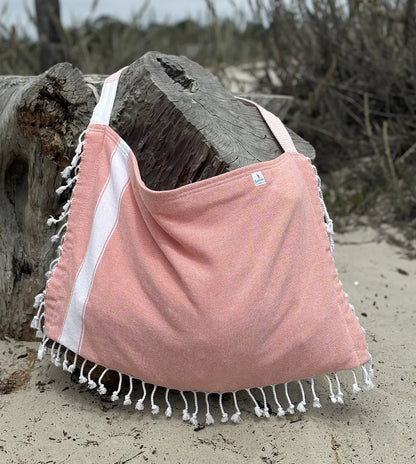 Coral bag with white trim draped over a log on a sandy beach.