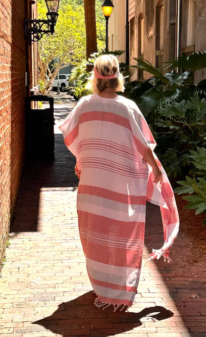 Person wearing a red, blue and white striped cover-up walking down a sunlit street.