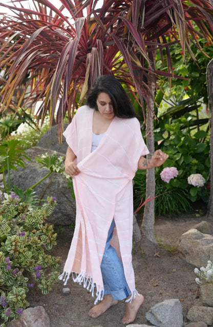 Woman in a peach long cover-up  standing in a garden with plants and flowers around.