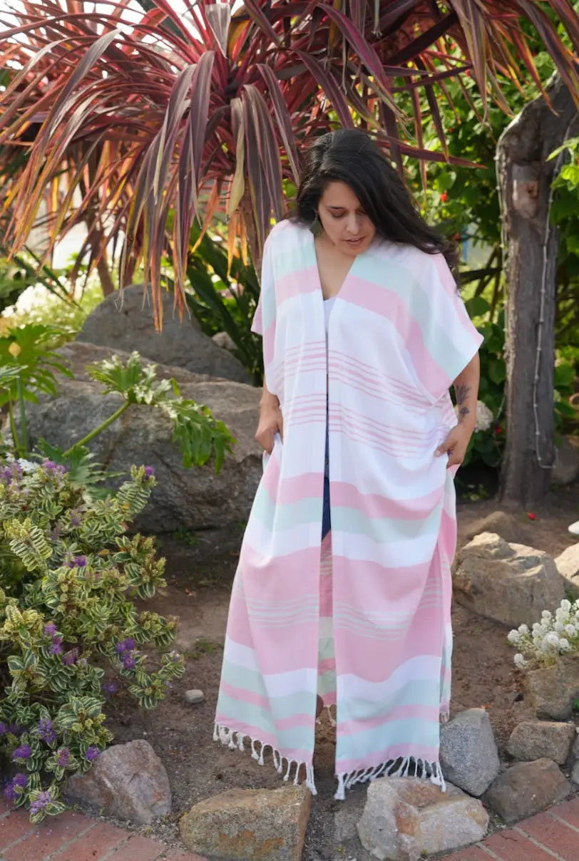 Woman wearing a pink and white striped cover-up  standing in a garden setting with plants and rocks.