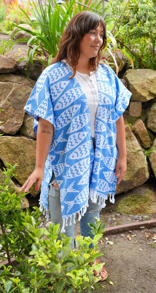 Woman wearing a blue patterned kimono-style garment standing outdoors near a stone wall.