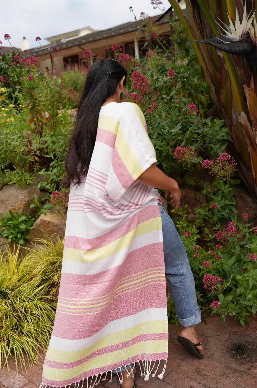Woman in a red, yellow and white striped kimono wrap walking through a garden with flowers and a building in the background