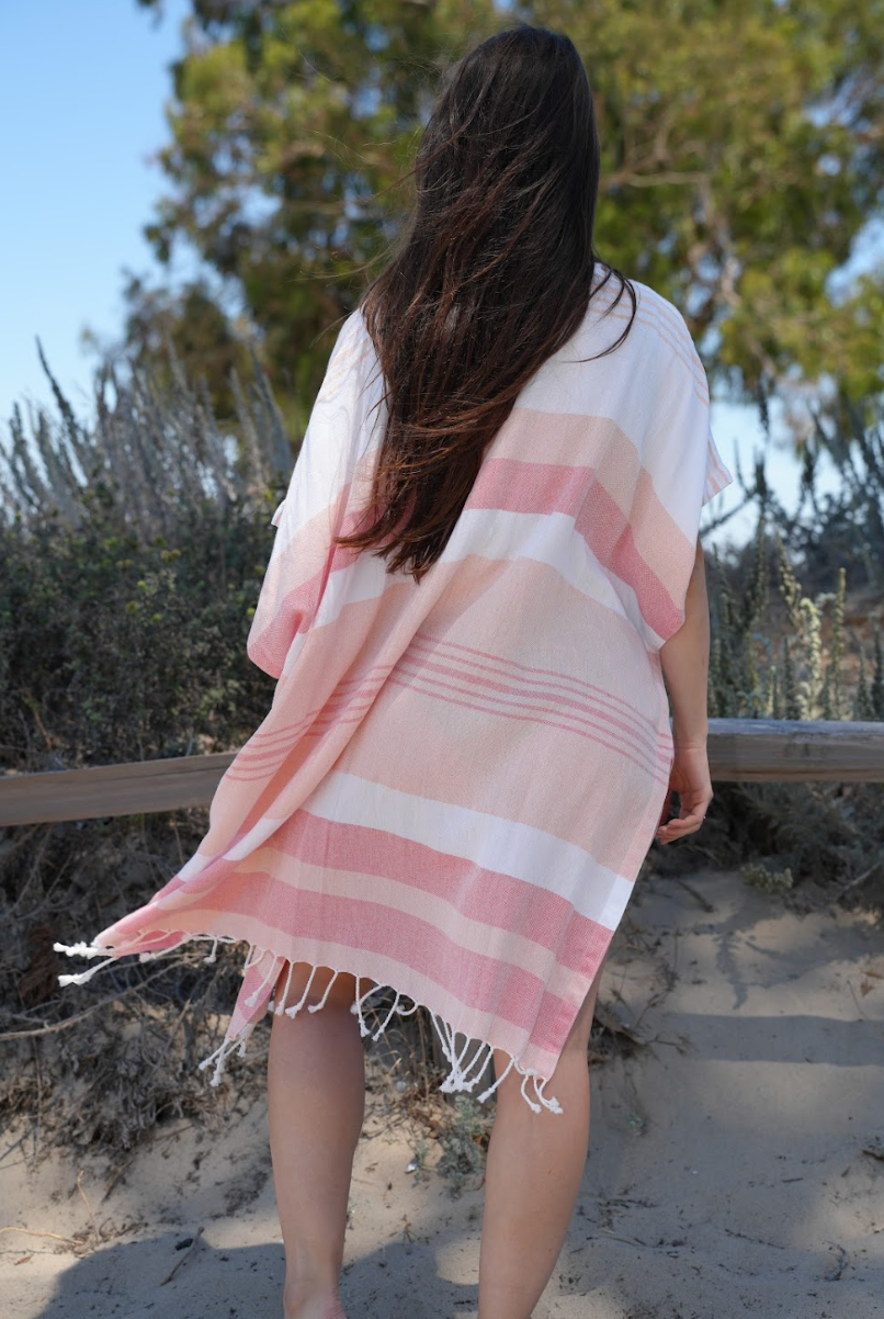 Back view of a woman in peach, red and white stripe mid-length cover-up in outdoor setting