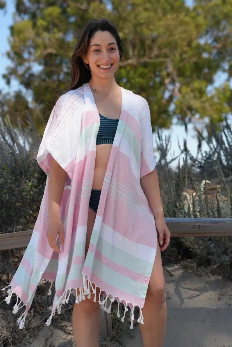 Woman on a beach wearing a green, pink and white striped cover-up with tassels