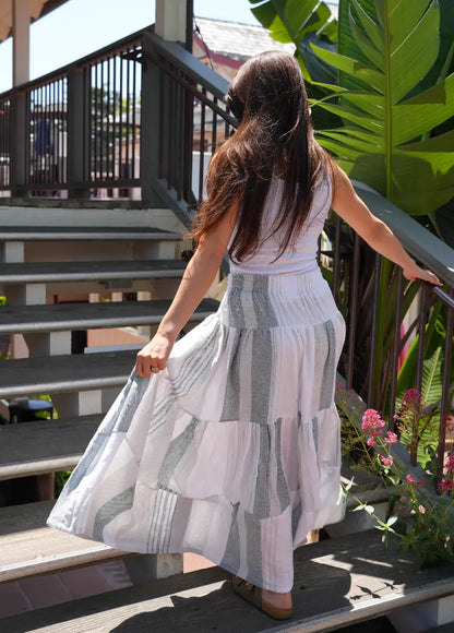 Back View of woman wearing a maxi length tiered skirt with charcoal, grey and white stripes with a white tank top outside 