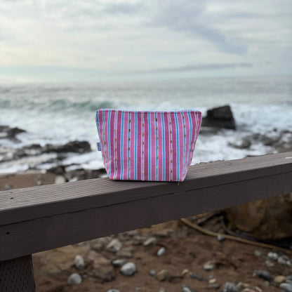 Pink Striped fabric pouch on a wooden bench with a beach background