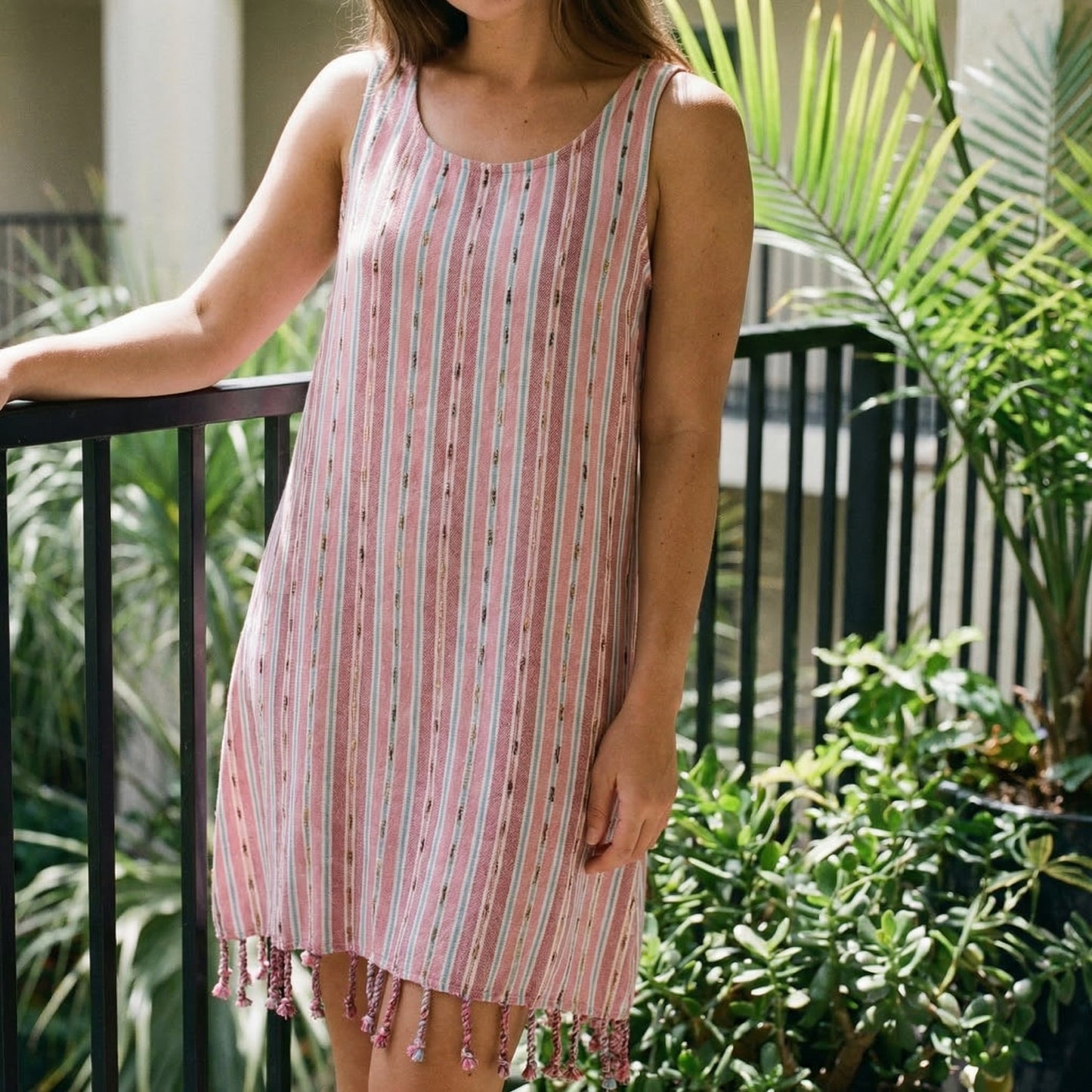 Woman wearing a pink and white striped dress with fringe on a balcony with plants in the background