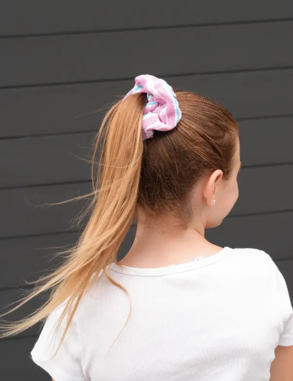 Person with pink scrunchie in ponytail against a gray wall