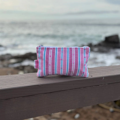 Pink and blue striped pouch on a wooden surface with a blurred ocean background