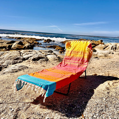 Colorful towel draped over a beach chair on a rocky beach with ocean waves in the background.