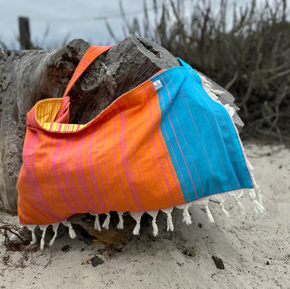 Orange and blue striped beach bag draped over a log on a sandy beach.