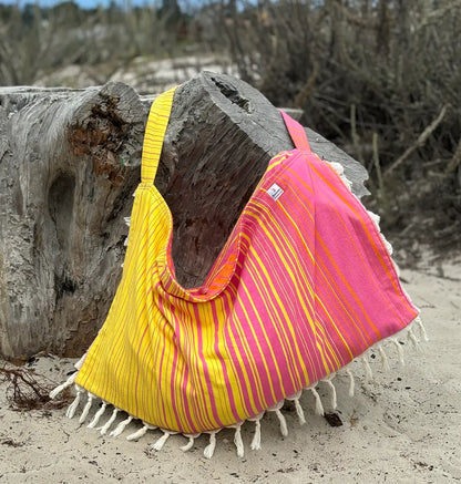 Yellow and pink striped bag with fringe on a sandy beach.