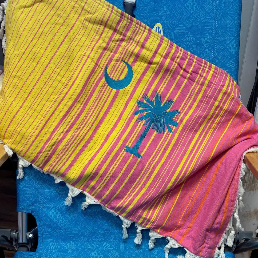 Colorful striped bag with palm tree and moon design on a blue chair.
