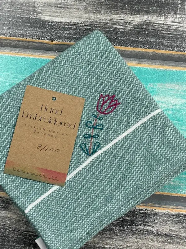 Green bandana with embroidered design and a brown tag on a textured surface