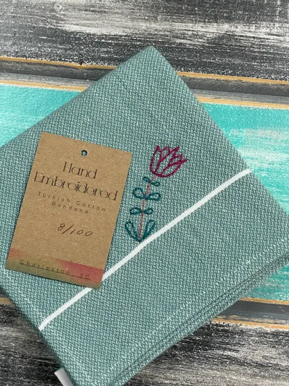 Green bandana with embroidered design and a brown tag on a textured surface