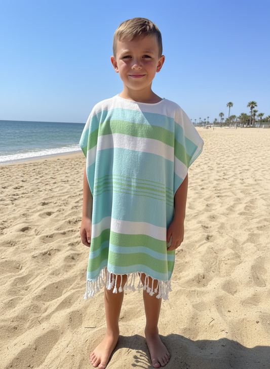 Child wearing a blue, green and white striped poncho on a sandy beach with ocean and sky in the background