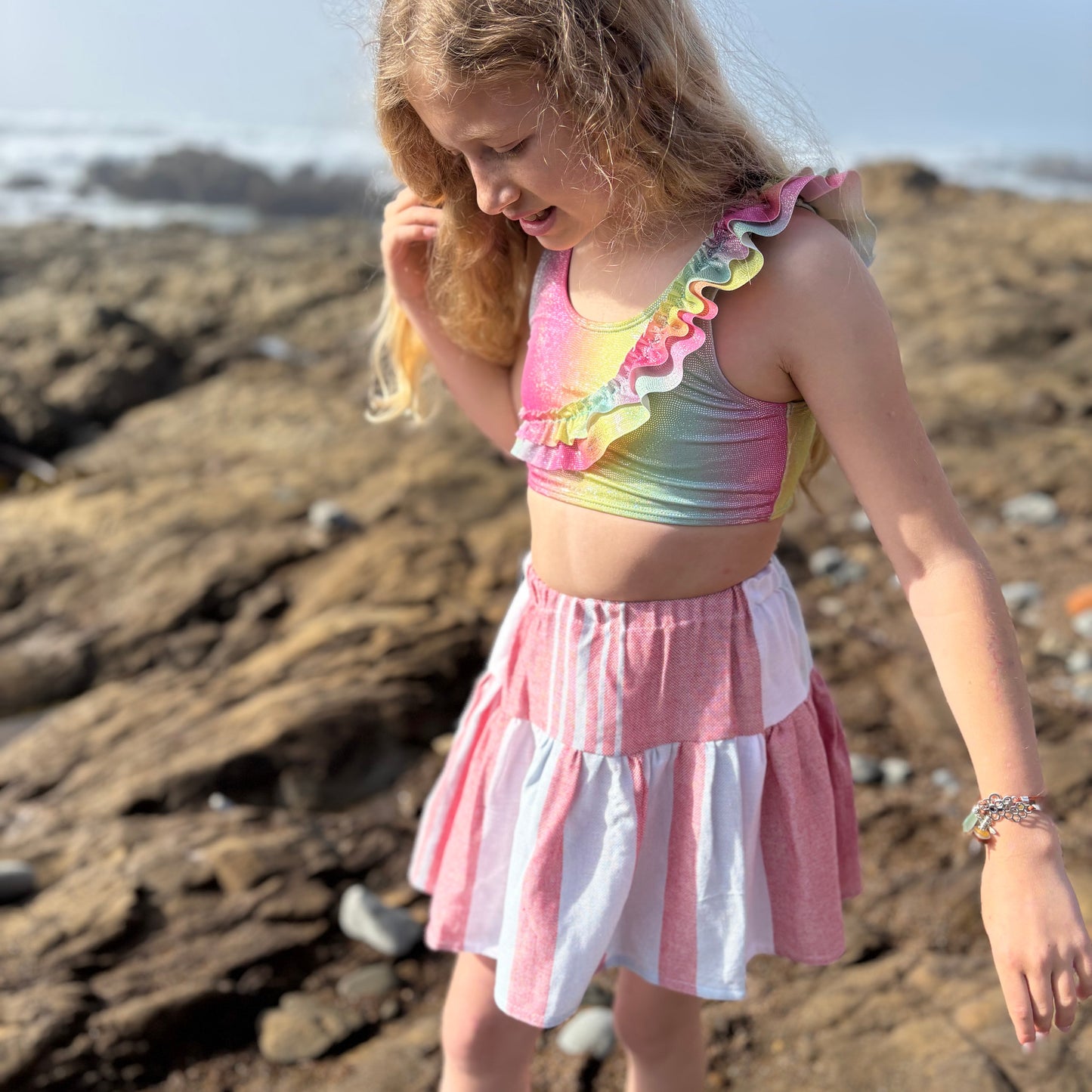 young girl wearing short tiered skirt with red, blue and white stripes walking on the beach