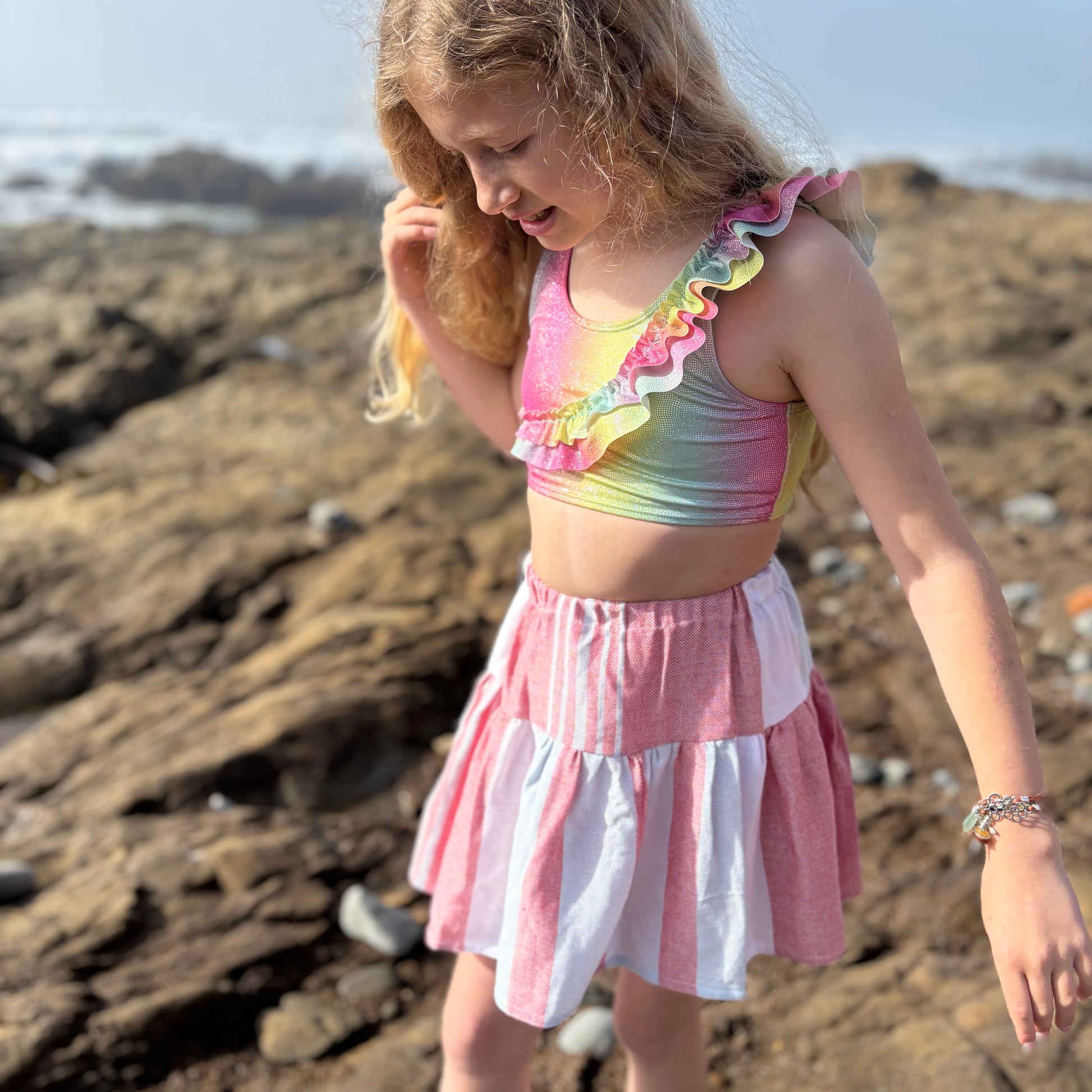 young girl wearing short tiered skirt with red, blue and white stripes walking on the beach
