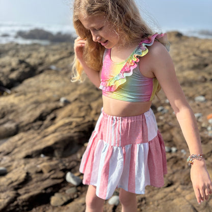 young girl wearing short tiered skirt with red, blue and white stripes walking on the beach