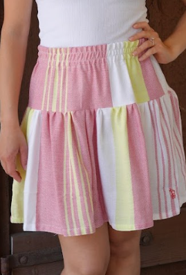 Close up of a short skirt with red, yellow and white stripes and a white tank top in front of a red door