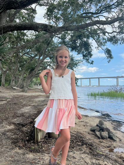 Young girl wearing a short tiered red, peach and white striped skirt posing near waterway with trees and a bridge in background