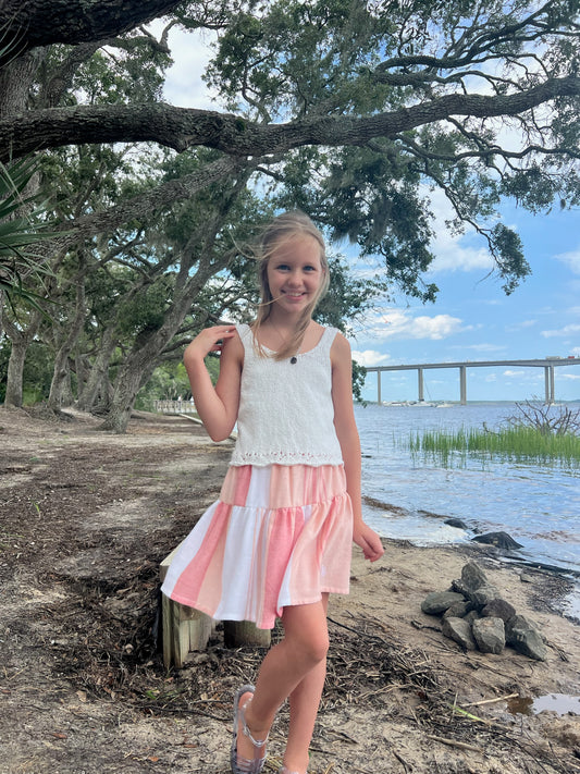 Young girl wearing a short tiered red, peach and white striped skirt posing near waterway with trees and a bridge in background