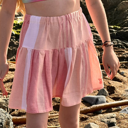 Close up of a young girl wearing short tiered skirt with red, peach and white stripes on the beach